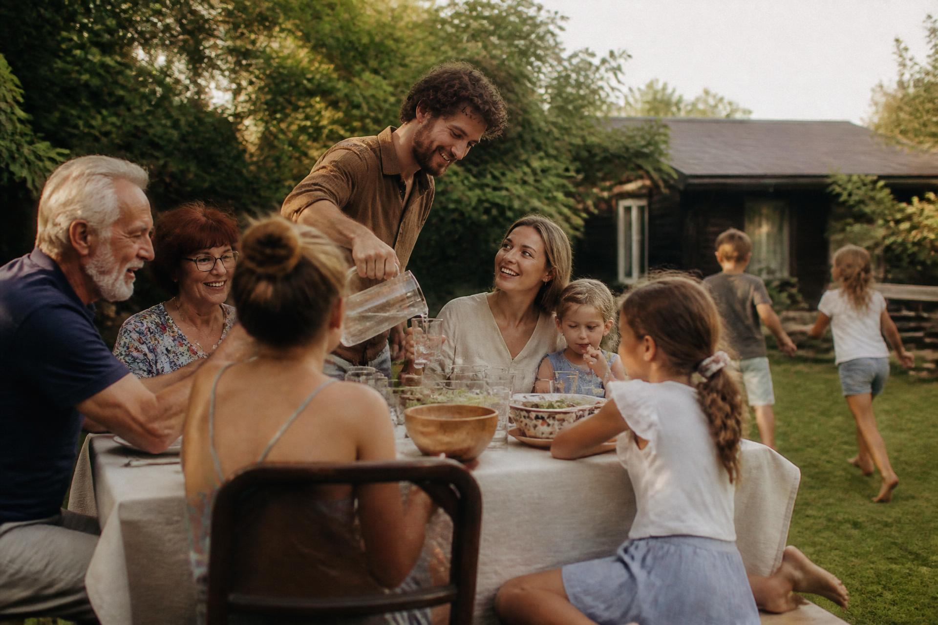 A family of all ages gathered around a long table in the garden of a family home